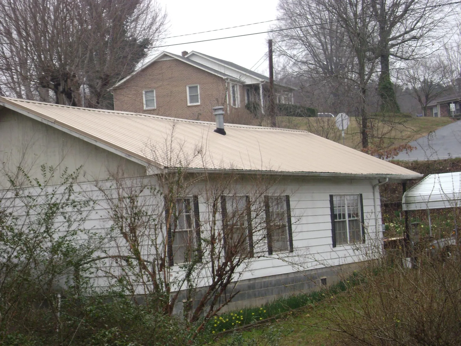 Tan metal roof on a white sided house set into a hillside — Commercial Roofing by Roofing Brothers in Ferndale
